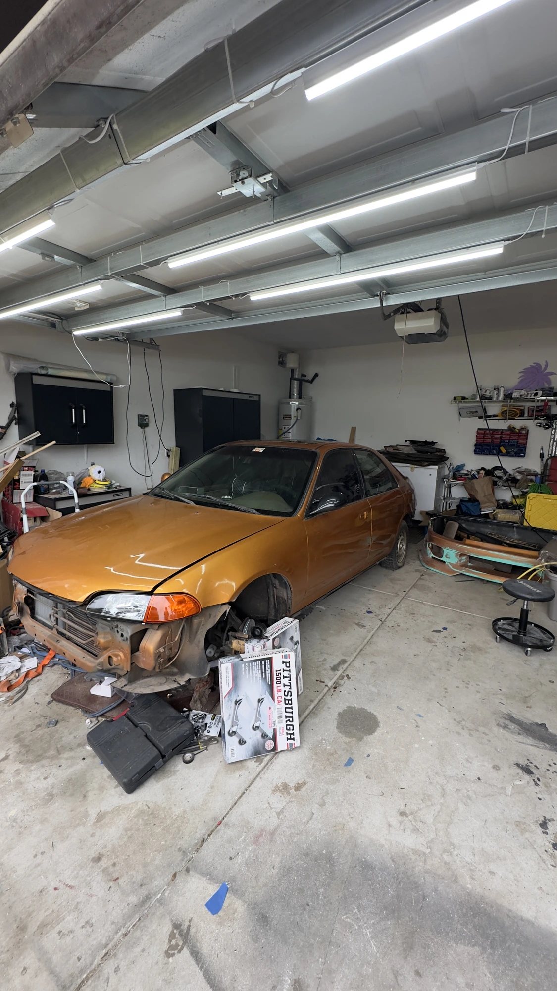 The Civic mid-strip in the garage — bumper and fender liner off, tools scattered