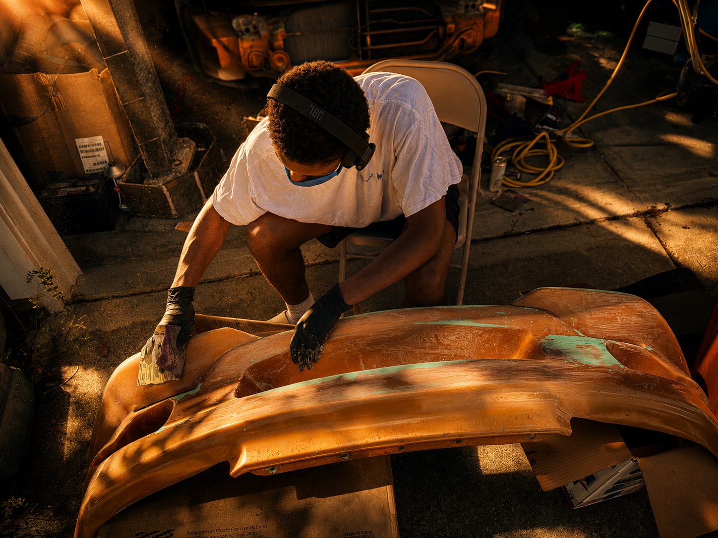 His son sanding the old body kit smooth in the sun outside the garage